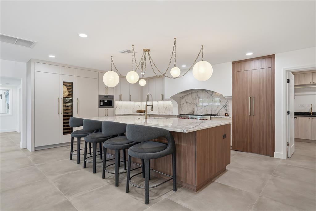 A modern kitchen features a large marble-topped island, dark bar stools, and wood-paneled cabinetry — 3896 42ND AVENUE S, ST PETERSBURG, FL
