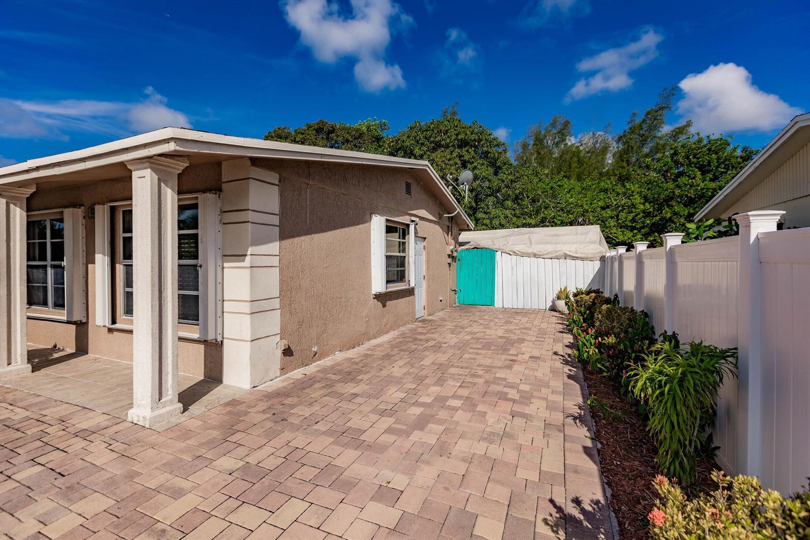 A tan house exterior features a paved patio, white columns, and a white privacy fence — 4241 NE 1st Terrace, Pompano Beach FL 33064, POMPANO BEACH, FL