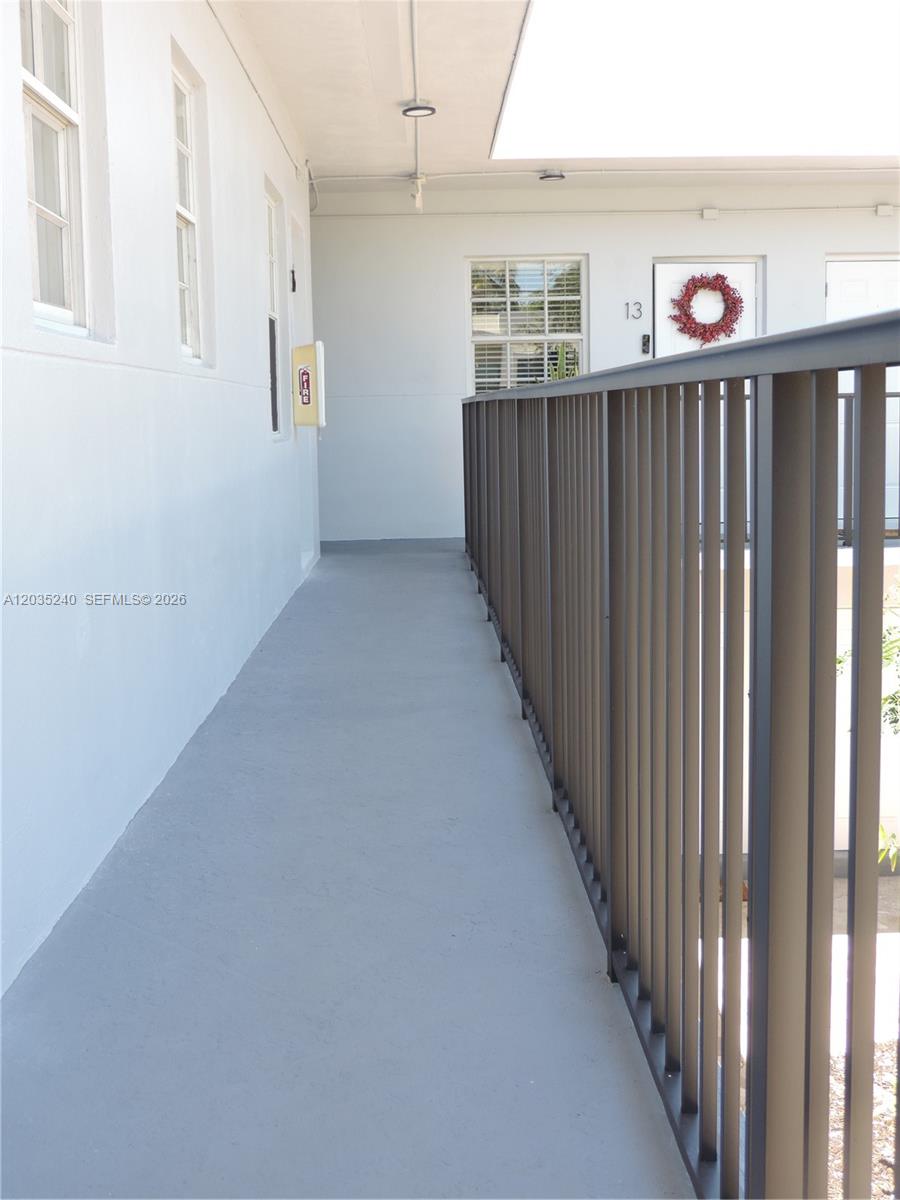 An outdoor walkway features a metal railing, white walls, and a door with a wreath — 3615 Thomas Ave # 11, Miami FL 33133, MIAMI, FL