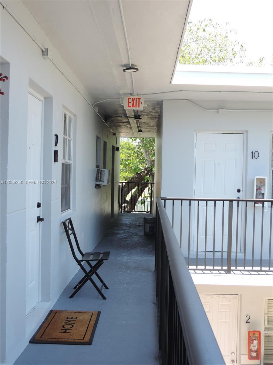 An outdoor apartment walkway features a metal railing, a chair, and numbered unit doors — 3615 Thomas Ave # 11, Miami FL 33133, MIAMI, FL