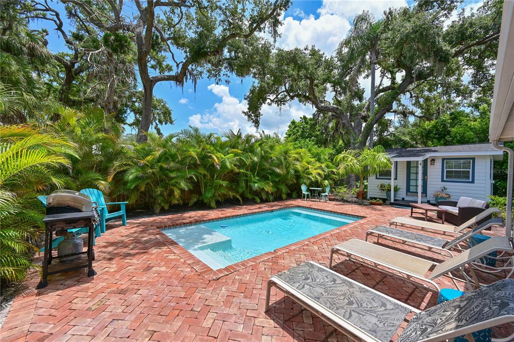 A backyard features a rectangular swimming pool surrounded by a red brick patio and landscaping — 1318 6TH STREET W, PALMETTO, FL