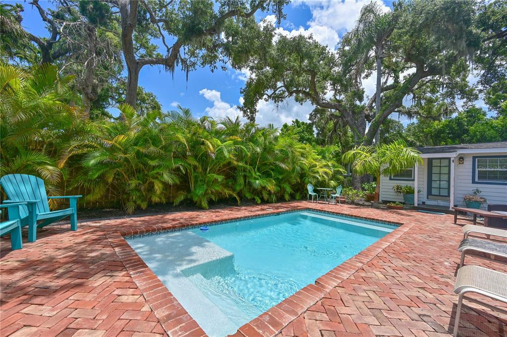 A backyard swimming pool with a brick patio, lounge chairs, and lush tropical landscaping — 1318 6TH STREET W, PALMETTO, FL