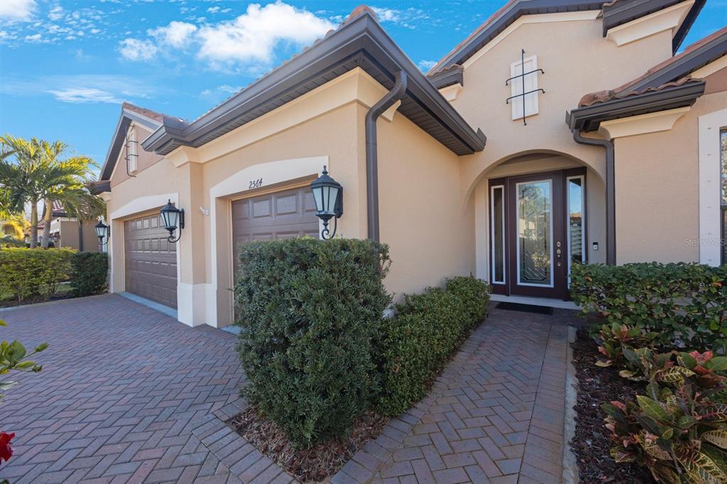 A beige house exterior with a brick driveway, a two-car garage, and a front entryway — 2564 GRAND CYPRESS BOULEVARD, PALM HARBOR, FL