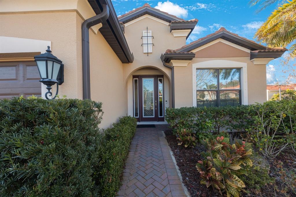 A brick walkway leads to the front entrance of a beige house with dark trim — 2564 GRAND CYPRESS BOULEVARD, PALM HARBOR, FL