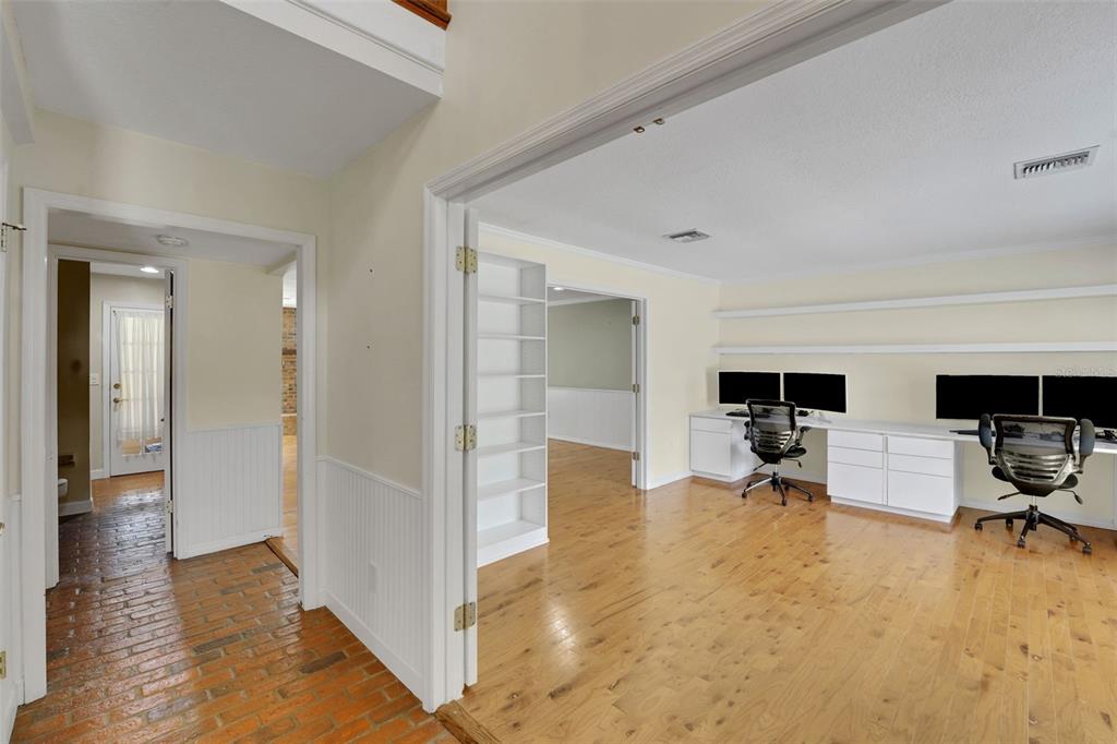 A home office with hardwood floors, a built-in desk, and shelving, adjacent to a brick hallway — 230 HUNTERS TRAIL, LONGWOOD, FL