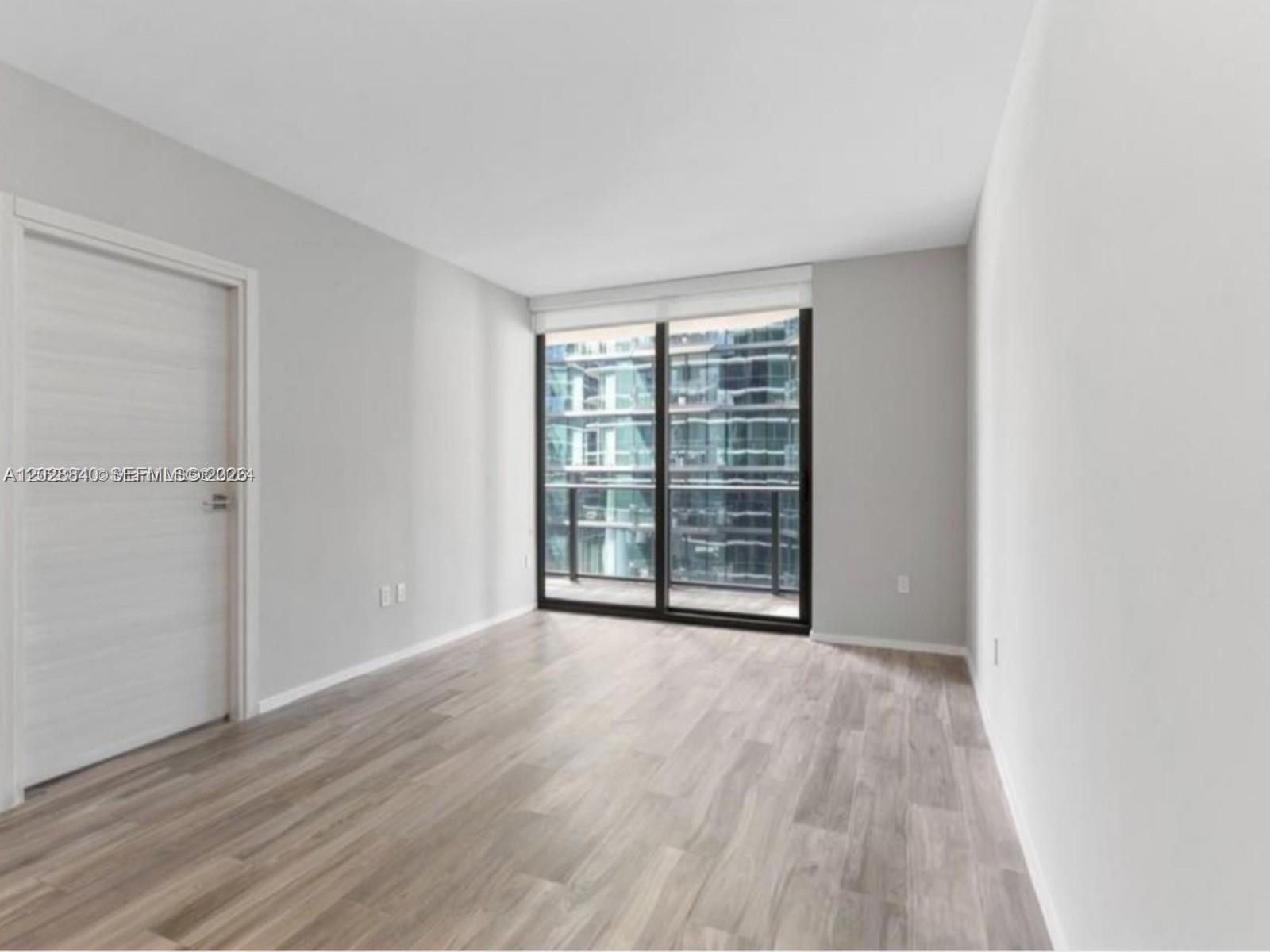 An empty room with light wood-look flooring, white walls, and a sliding glass balcony door — 801 S Miami Ave # 1808, Miami FL 33130, MIAMI, FL