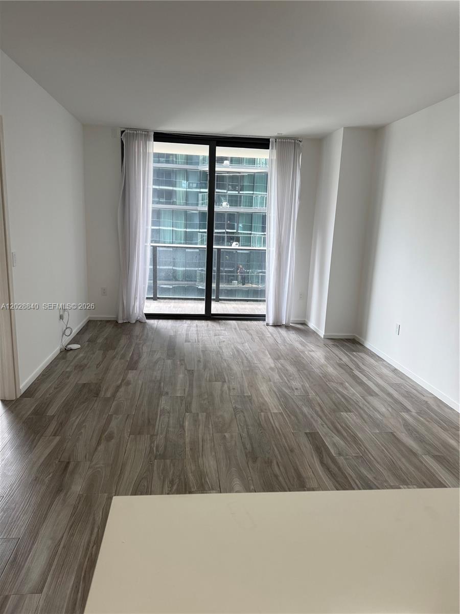An empty room features light wood-look flooring, white walls, and a sliding glass balcony door — 801 S Miami Ave # 1808, Miami FL 33130, MIAMI, FL