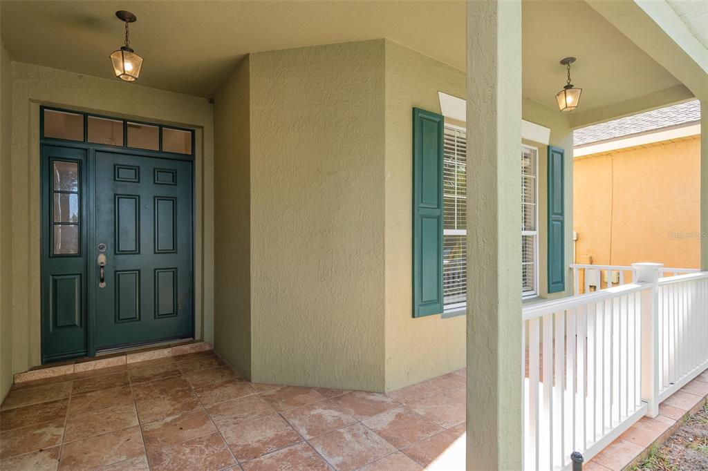 A covered front porch with tiled flooring, a dark green door, and white railings — 1513 HARRIER DRIVE, ORLANDO, FL