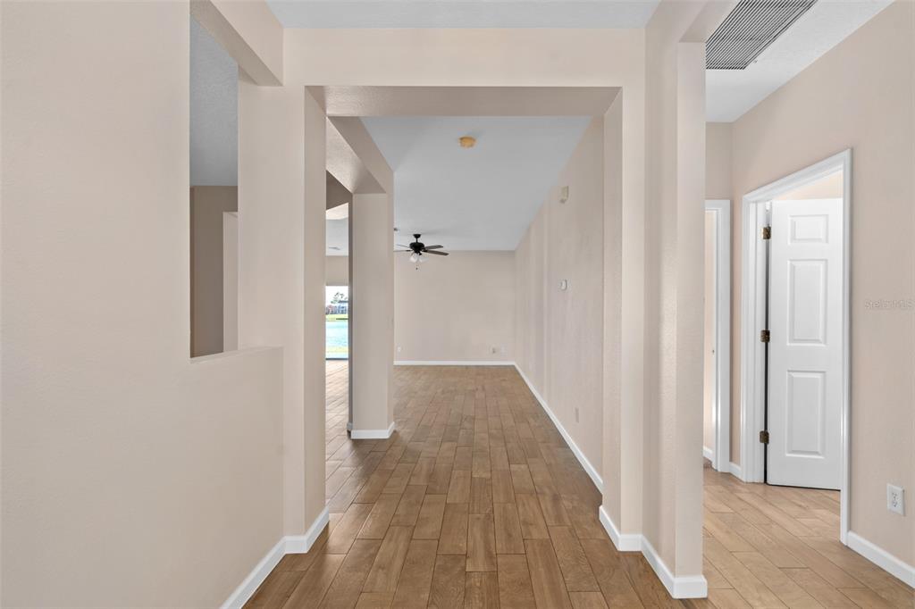 A hallway with wood-look tile flooring leads toward an open living area with a ceiling fan — 1513 HARRIER DRIVE, ORLANDO, FL