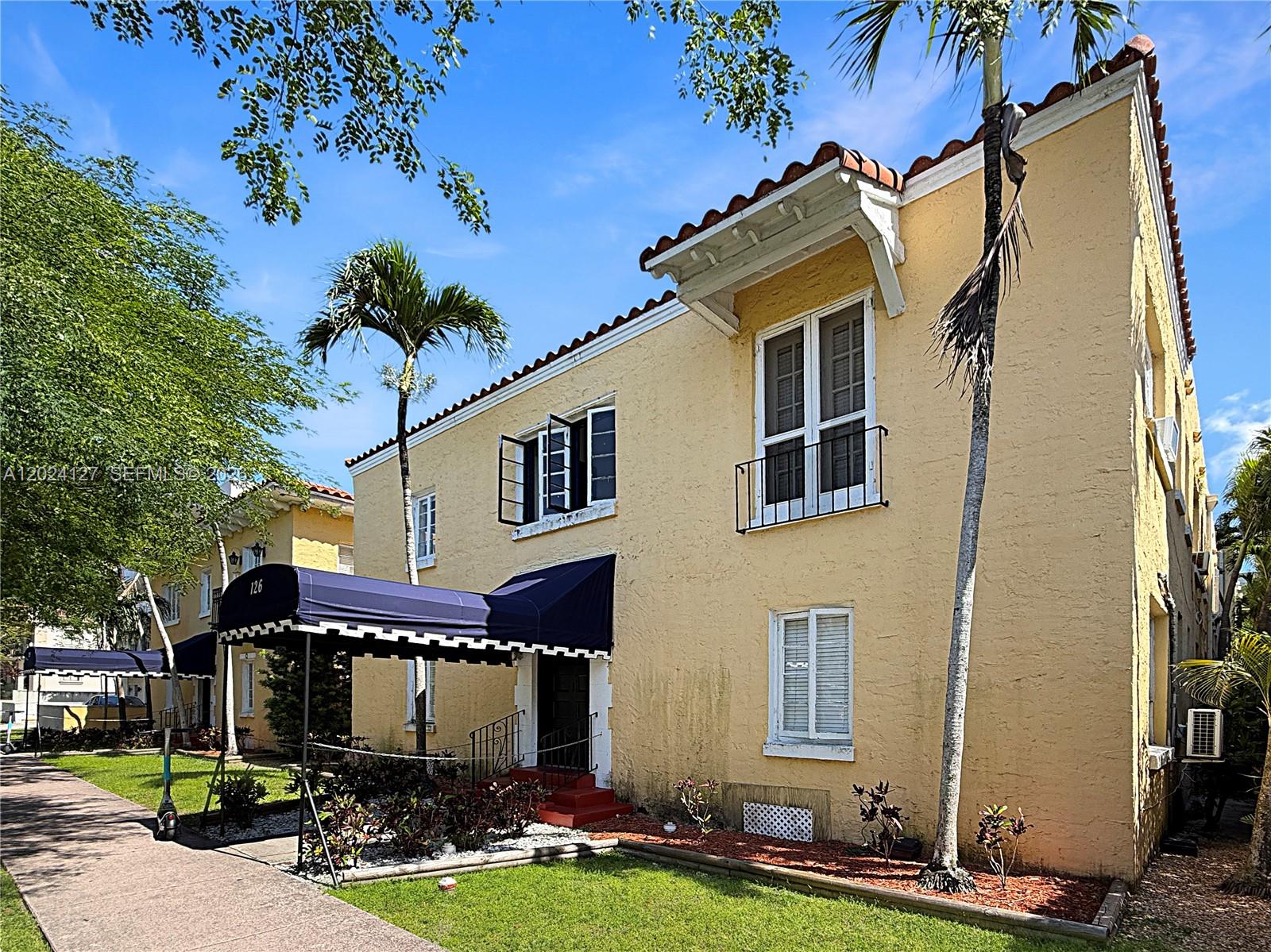 A yellow two-story building features a blue awning over the entrance and palm trees — 126 Mendoza Ave # 7A, Coral Gables FL 33134, CORAL GABLES, FL