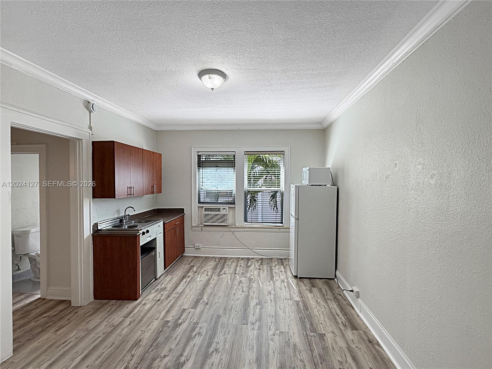 A small kitchen features wood cabinets, a white refrigerator, and light wood-look flooring — 126 Mendoza Ave # 7A, Coral Gables FL 33134, CORAL GABLES, FL
