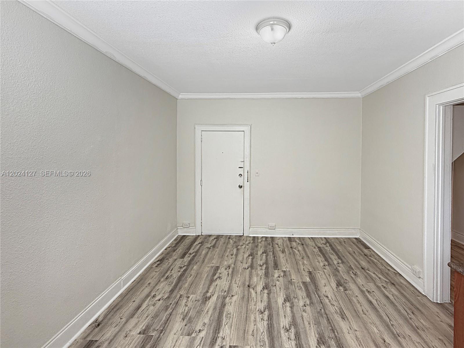 An empty room features light gray walls, white trim, and wood-look laminate flooring — 126 Mendoza Ave # 7A, Coral Gables FL 33134, CORAL GABLES, FL