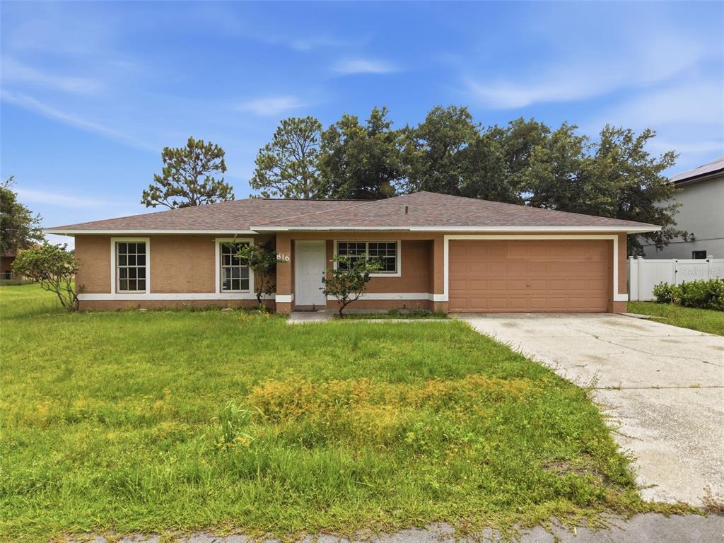 A single-story house with a tan stucco exterior, a two-car garage, and a front lawn — 816 ADOUR DRIVE, KISSIMMEE, FL