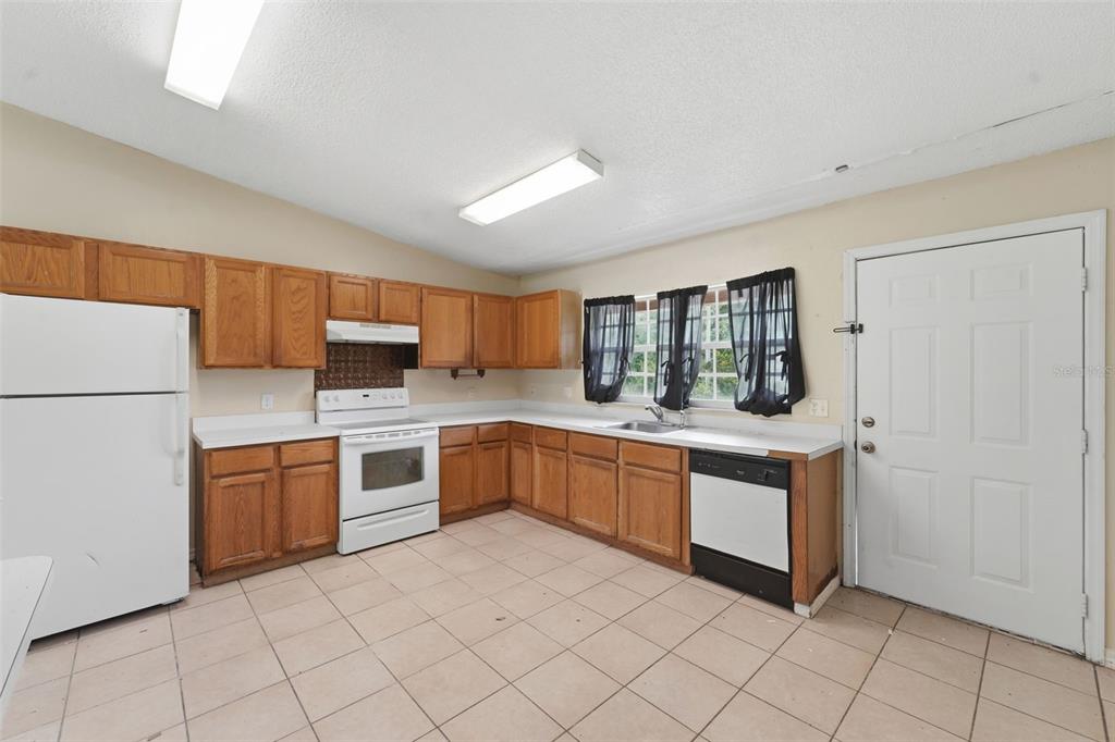 A kitchen with wood cabinets, white appliances, tile flooring, and a white exterior door — 816 ADOUR DRIVE, KISSIMMEE, FL
