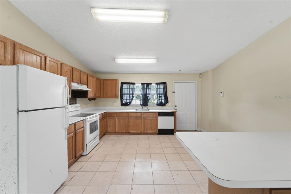 A kitchen features wood cabinets, white appliances, tile flooring, and a white countertop island — 816 ADOUR DRIVE, KISSIMMEE, FL