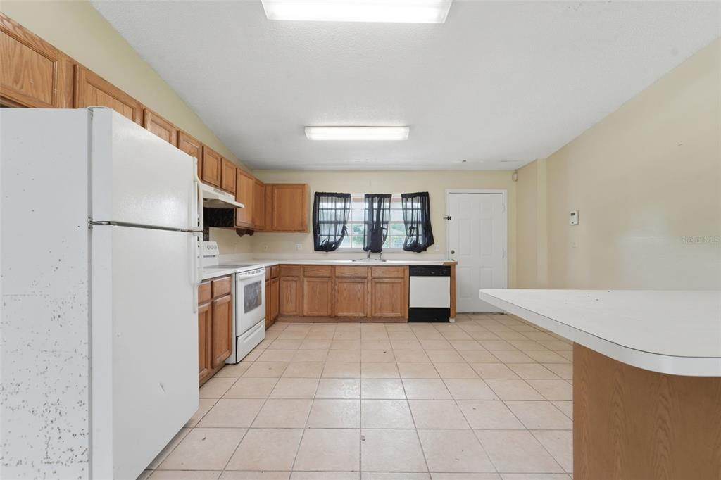 A kitchen features light-colored tile flooring, wood cabinets, white appliances, and a peninsula counter — 816 ADOUR DRIVE, KISSIMMEE, FL
