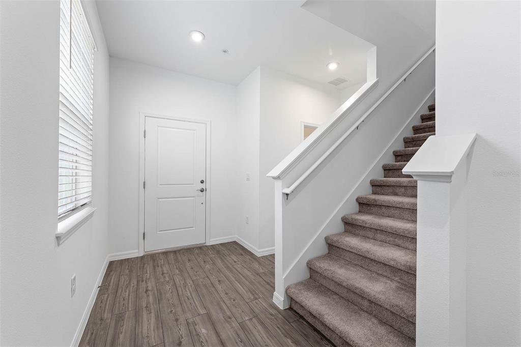 An entryway features wood-look flooring, a white front door, and carpeted stairs with a railing — 4692 INNER WORLD LANE, WESLEY CHAPEL, FL