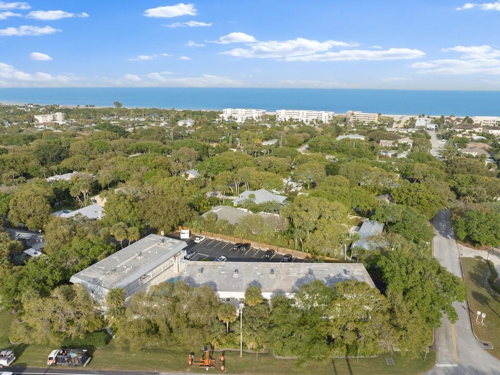 An aerial view shows a low-rise apartment building surrounded by trees near the ocean — 900 Jasmine Lane # 10a, Vero Beach FL 32963, VERO BEACH, FL