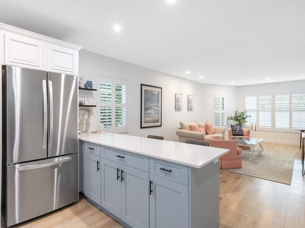 A kitchen island with light blue cabinets and a white countertop faces a living room — 900 Jasmine Lane # 10a, Vero Beach FL 32963, VERO BEACH, FL