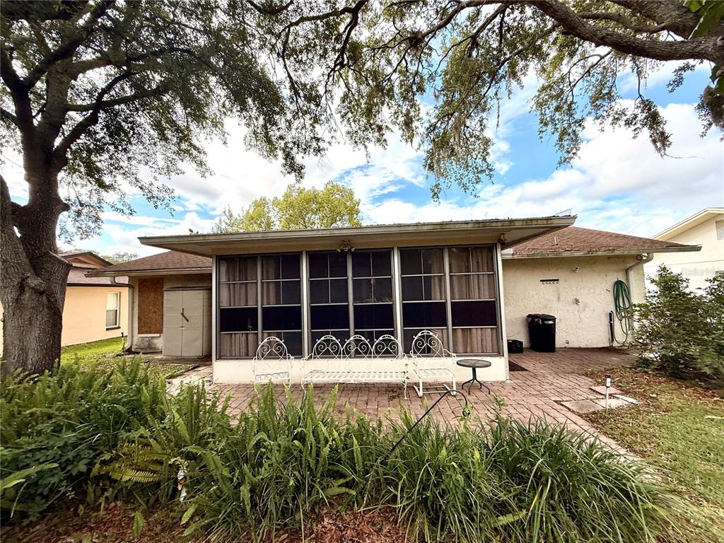 A screened-in porch with white metal furniture sits on a brick patio behind a house — 8634 WINDING WOOD DRIVE, PORT RICHEY, FL