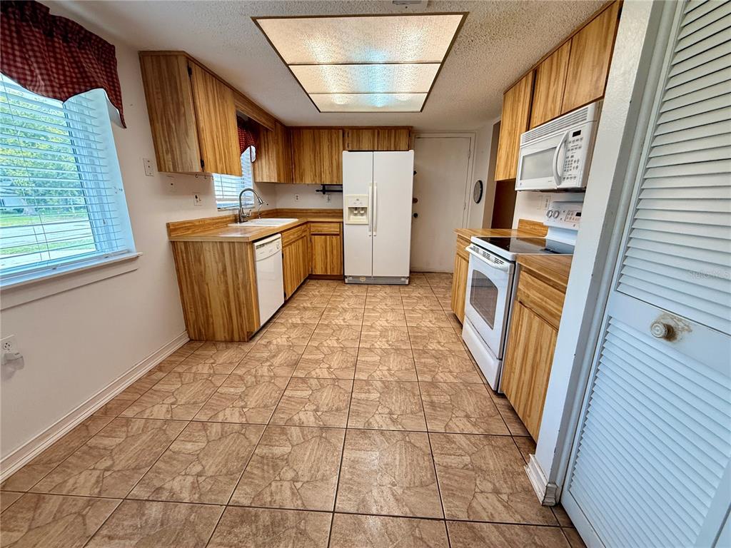 A kitchen features wood cabinets, white appliances, tiled flooring, and a large rectangular ceiling light — 8634 WINDING WOOD DRIVE, PORT RICHEY, FL