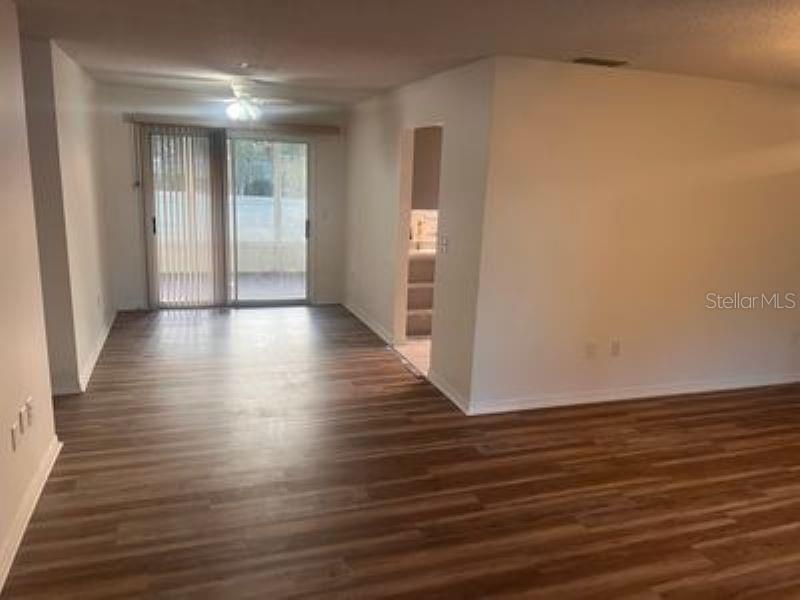 An empty living area with wood-look flooring, a ceiling fan, and sliding glass patio doors — 17624 SE 108TH TERRACE, SUMMERFIELD, FL