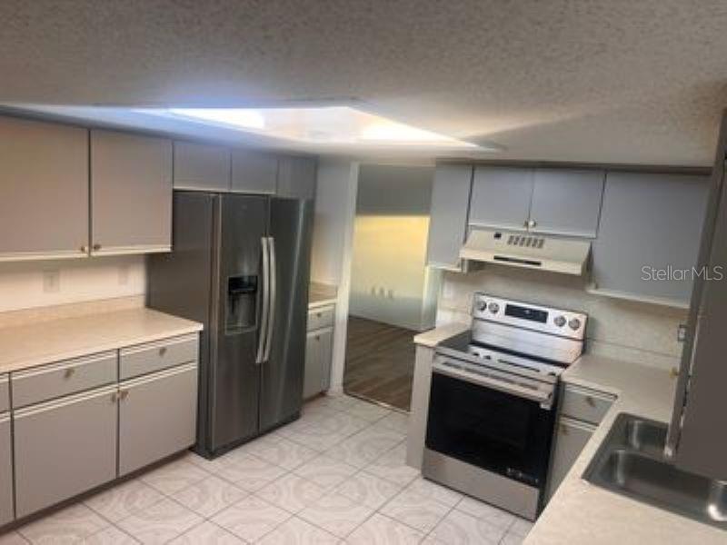 A kitchen with grey cabinets, stainless steel appliances, light countertops, and tiled flooring — 17624 SE 108TH TERRACE, SUMMERFIELD, FL