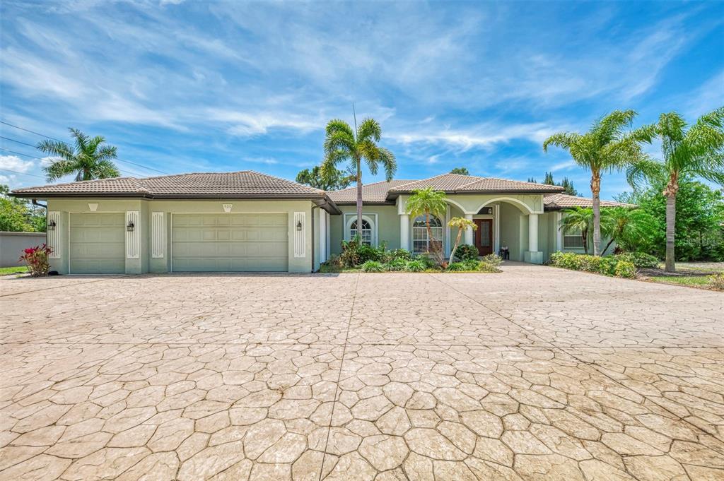 A single-story house with a large stamped concrete driveway, a three-car garage, and palm trees — 900 PARK PLACE DRIVE, ENGLEWOOD, FL