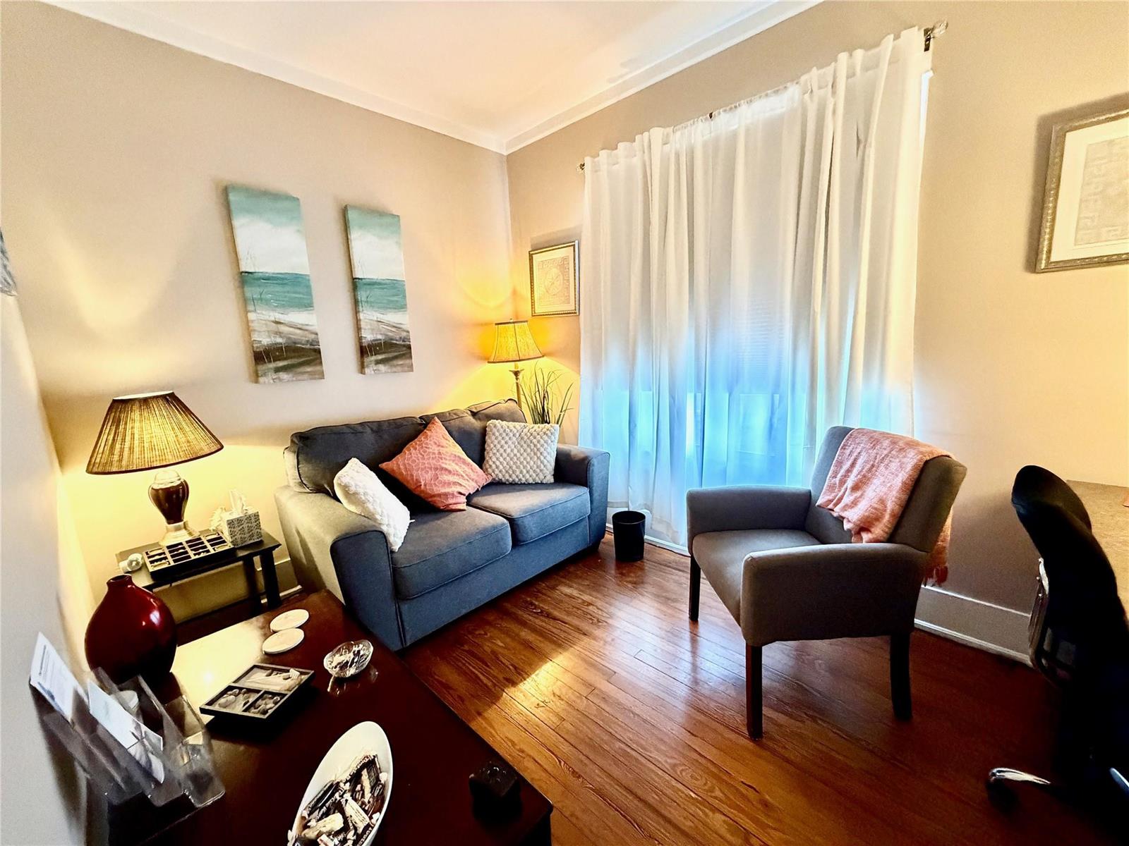 A living room features a gray sofa, an armchair, hardwood floors, and white curtains — 1925 20th Street, Vero Beach FL 32960, VERO BEACH, FL