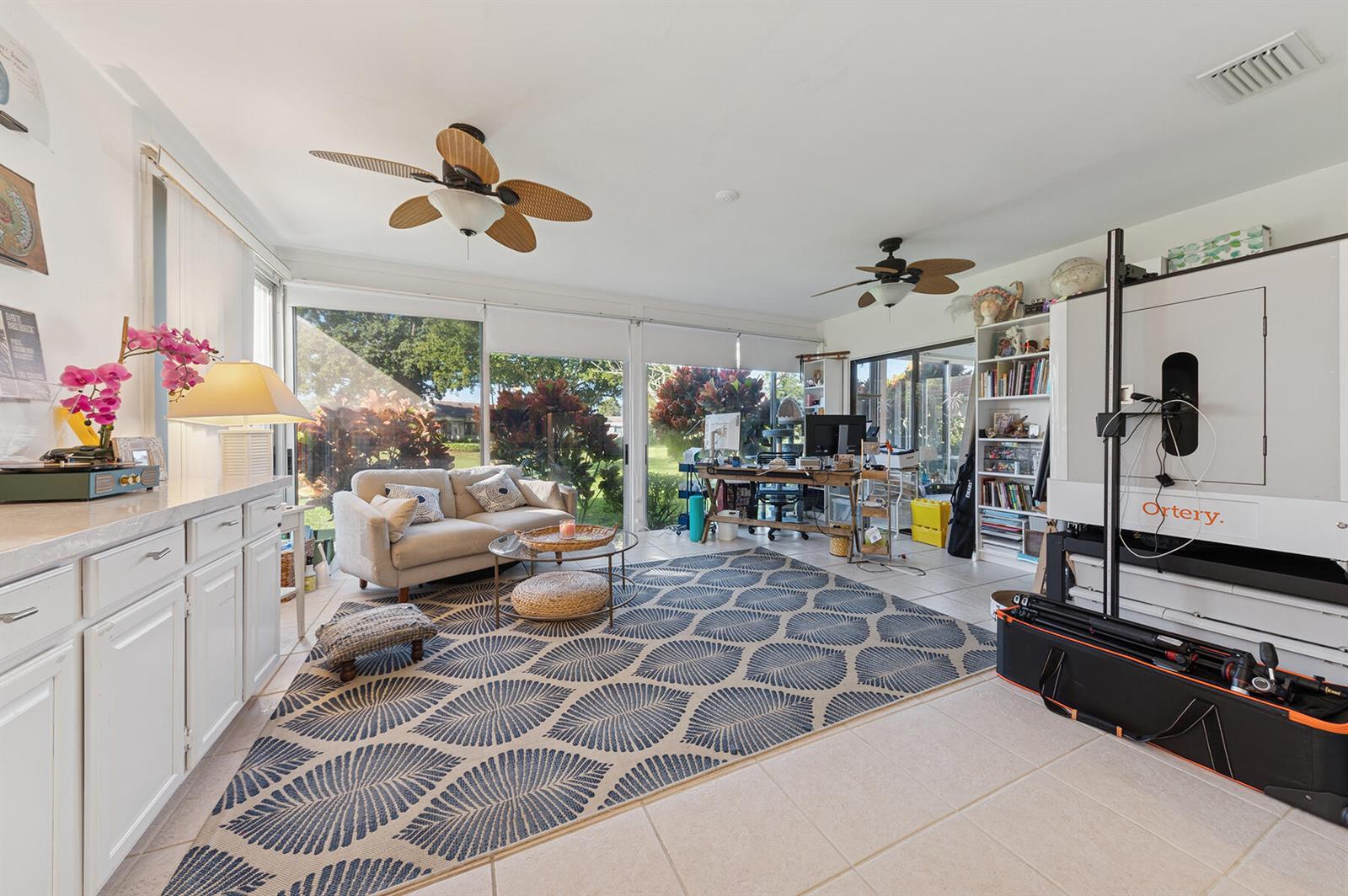 A sunroom features a large patterned area rug, a sofa, a desk, and floor-to-ceiling windows — 13 Fairway, Boynton Beach FL 33436, BOYNTON BEACH, FL