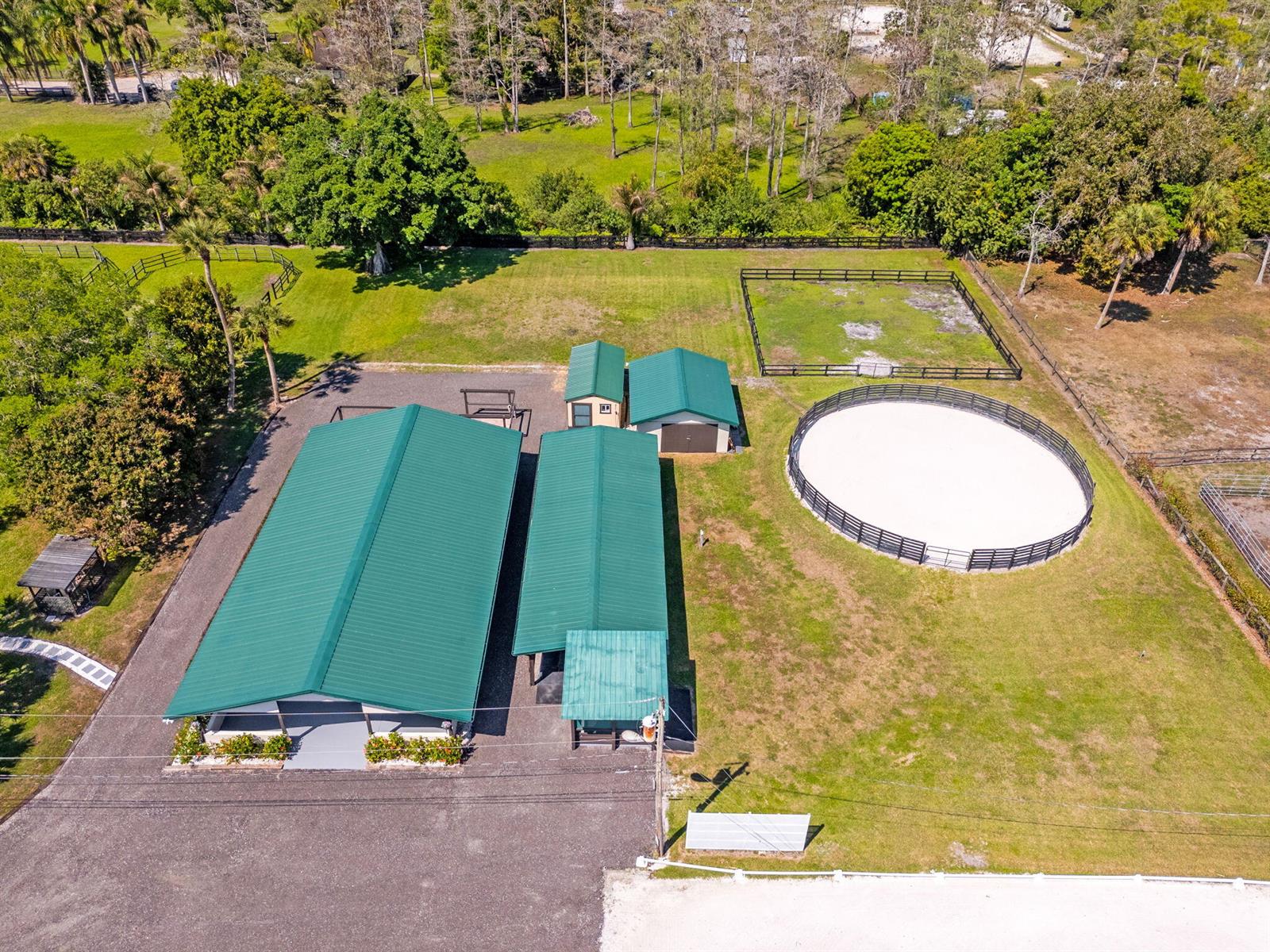 An aerial view shows a horse property with two green-roofed barns and a round pen — 1230 F Road, FL 33470, FL