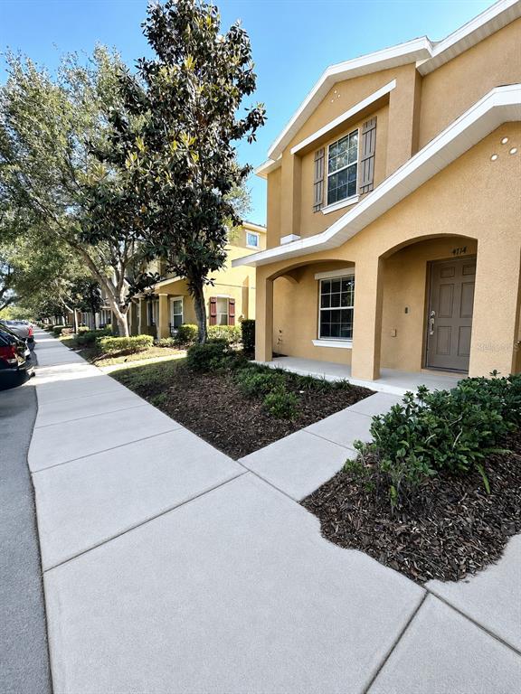 A two-story tan stucco townhouse with a front porch and a sidewalk leading to the entrance — 4714 CHATTERTON WAY, RIVERVIEW, FL