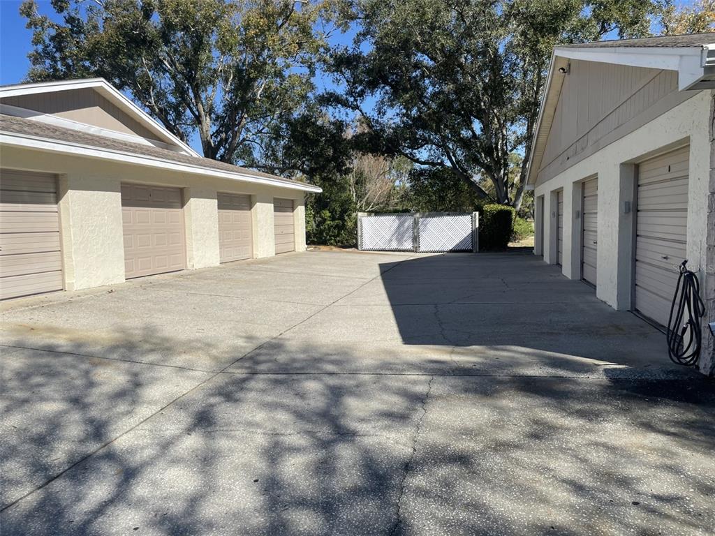 A paved driveway sits between two buildings featuring multiple garage doors and a white fence — 1084 DUNROBIN DRIVE UNIT D, PALM HARBOR, FL