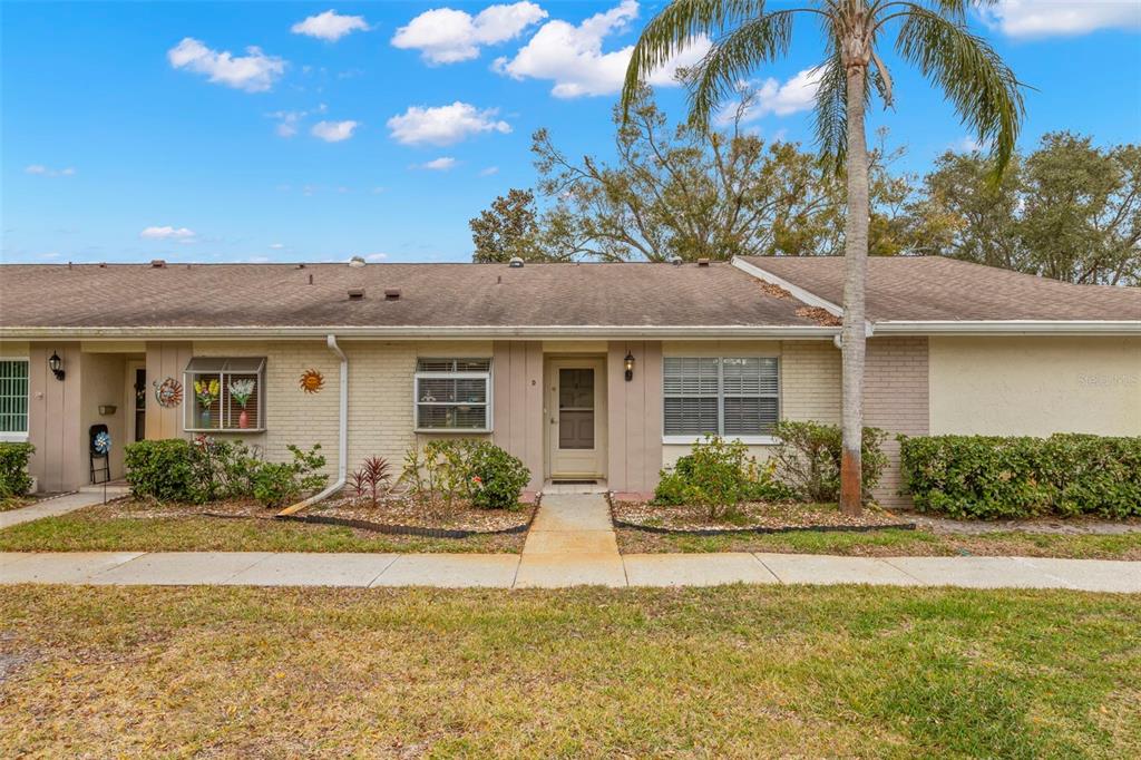 A single-story residential building with a tan brick facade, a palm tree, and a sidewalk — 1084 DUNROBIN DRIVE UNIT D, PALM HARBOR, FL