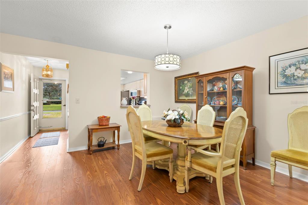 A dining room features a wooden table, cane-back chairs, a china cabinet, and wood flooring — 1084 DUNROBIN DRIVE UNIT D, PALM HARBOR, FL