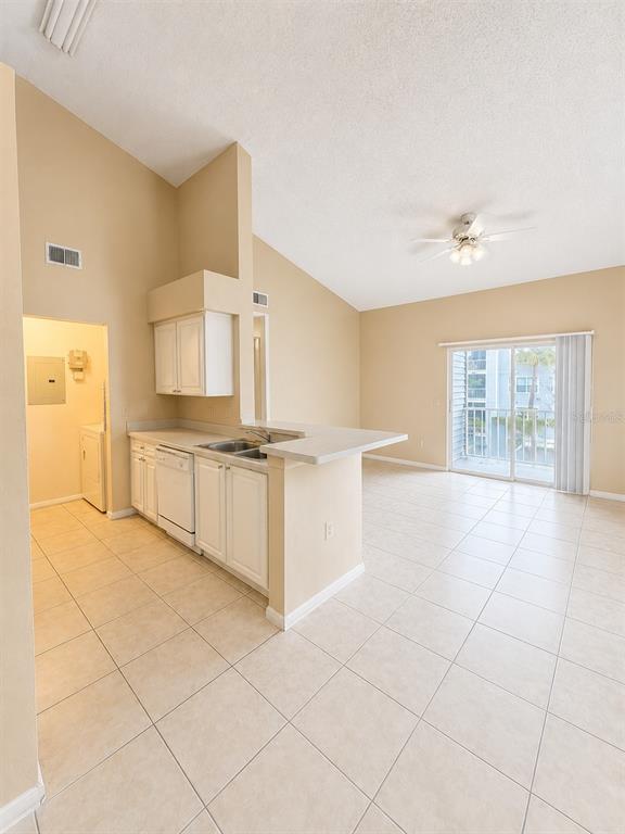 A kitchen with white cabinets and tile flooring opens into a living area with vaulted ceilings — 1218 BERMUDA LAKES LANE UNIT 201, KISSIMMEE, FL
