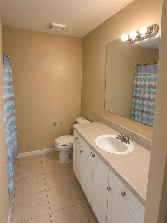 A bedroom features beige walls, tile flooring, a black bed, and a television on a stand — 1218 BERMUDA LAKES LANE UNIT 201, KISSIMMEE, FL