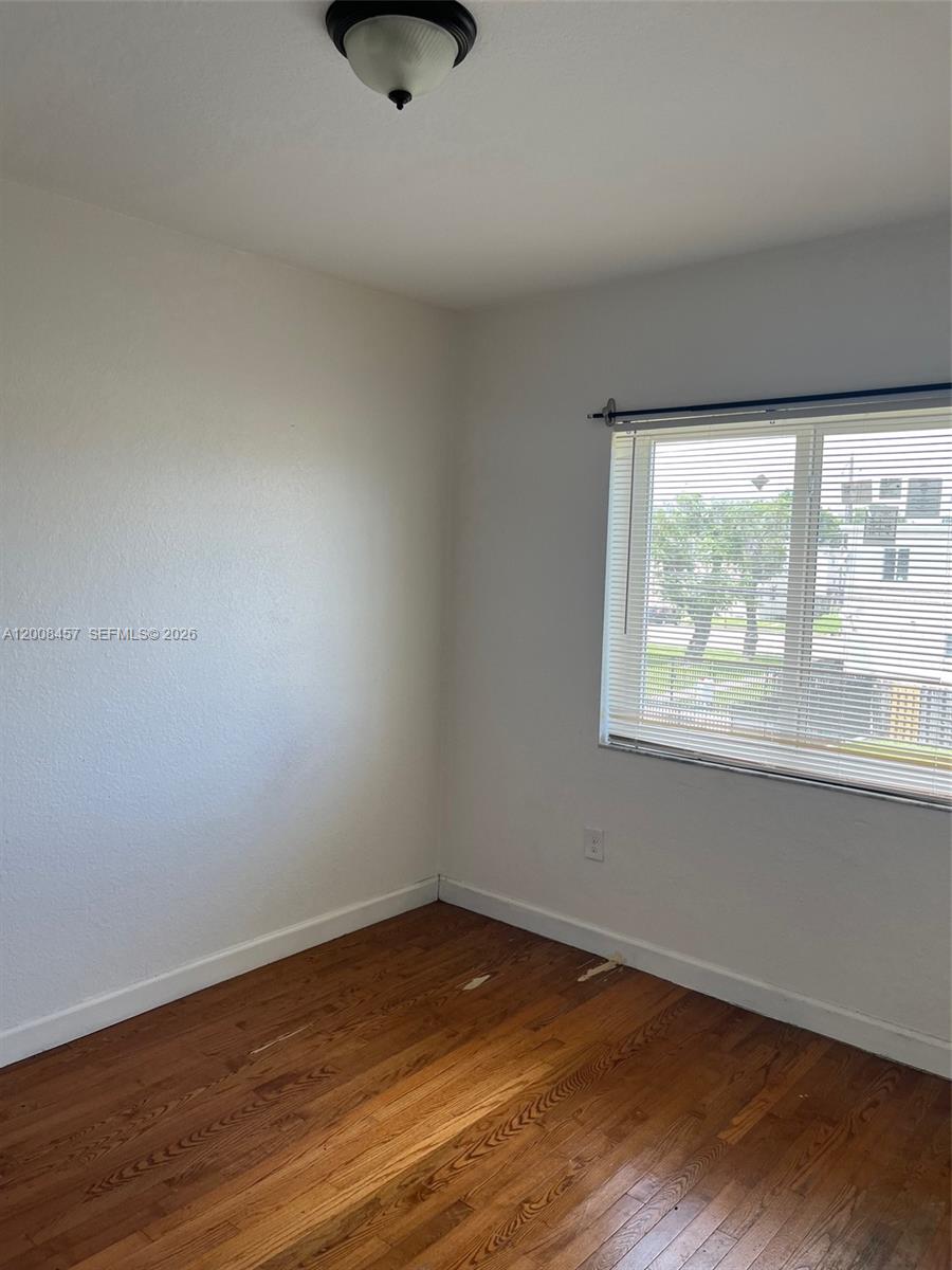 An empty room features hardwood flooring, white walls, a window with blinds, and a ceiling light — 403 NW 84th St # 403, Miami FL 33150, MIAMI, FL