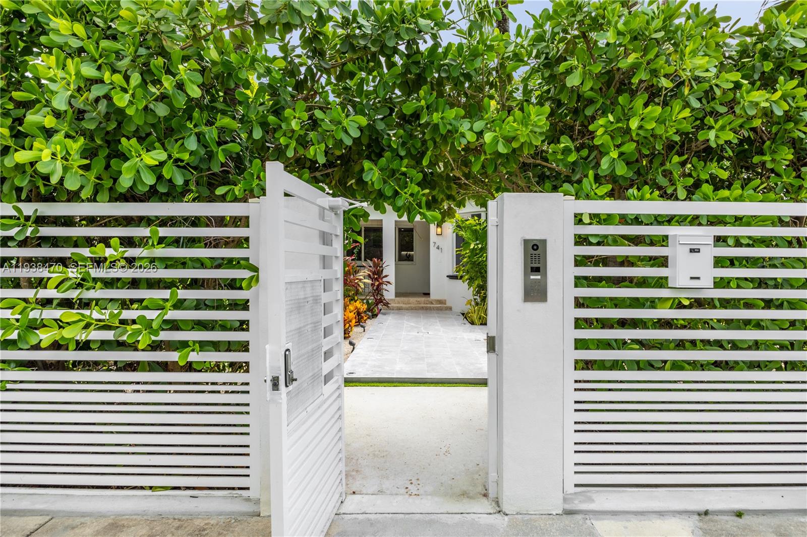 A white horizontal slat fence with an open gate leads to a paved walkway — 741 NE 87th St, Miami FL 33138, MIAMI, FL