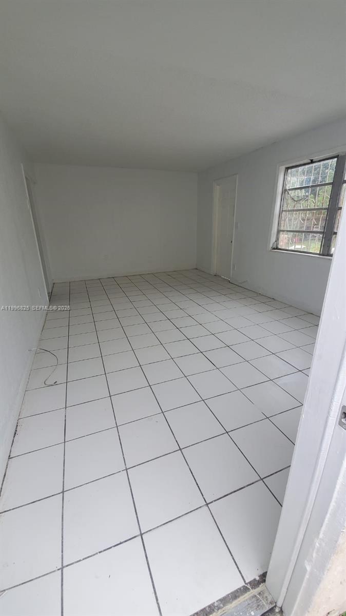 An empty room features white walls, white floor tiles, and a window with security bars — 2980 NW 91st St # 1, Miami FL 33147, MIAMI, FL