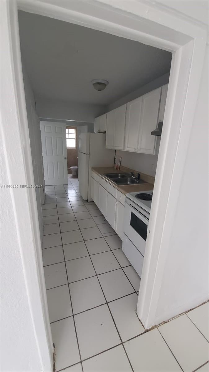 A galley-style kitchen features white cabinets, white appliances, and light-colored floor tiles — 2980 NW 91st St # 1, Miami FL 33147, MIAMI, FL