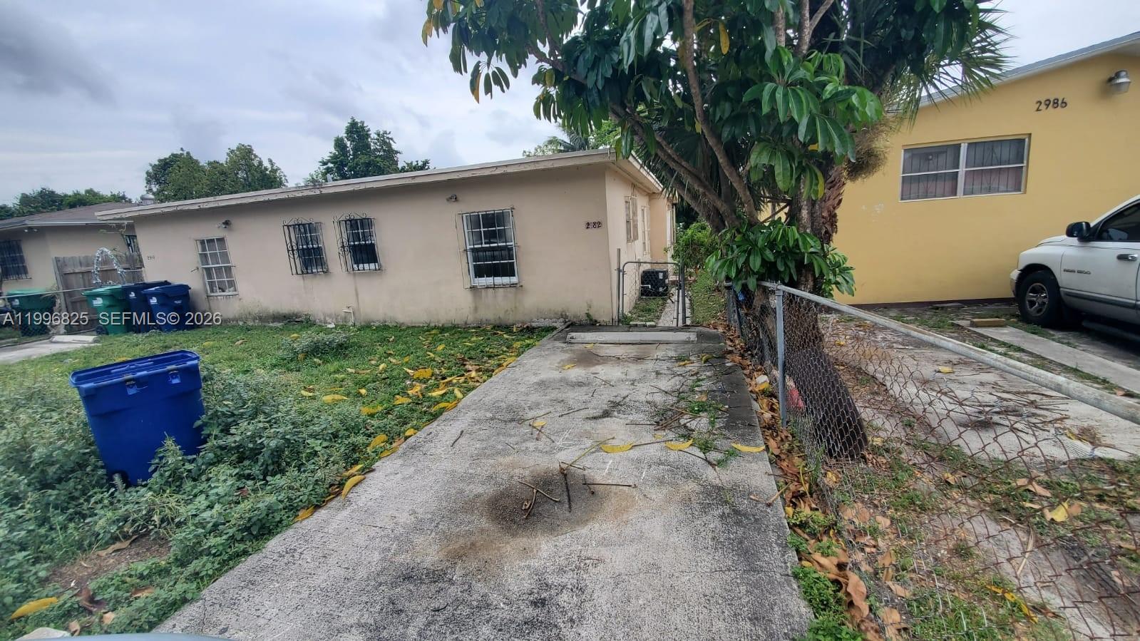 A concrete driveway leads toward a beige house with barred windows and a chain-link fence — 2980 NW 91st St # 1, Miami FL 33147, MIAMI, FL