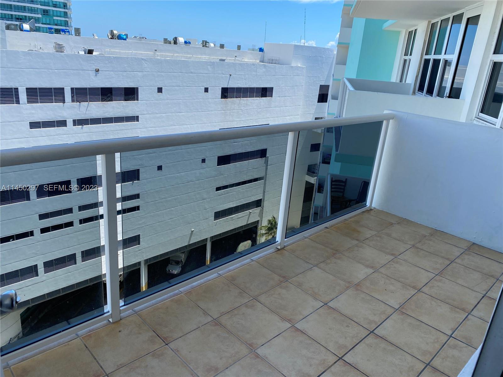 A balcony with tiled flooring and a glass railing overlooks a large white building — 3725 S Ocean Dr # 1521, Hollywood FL 33019, HOLLYWOOD, FL