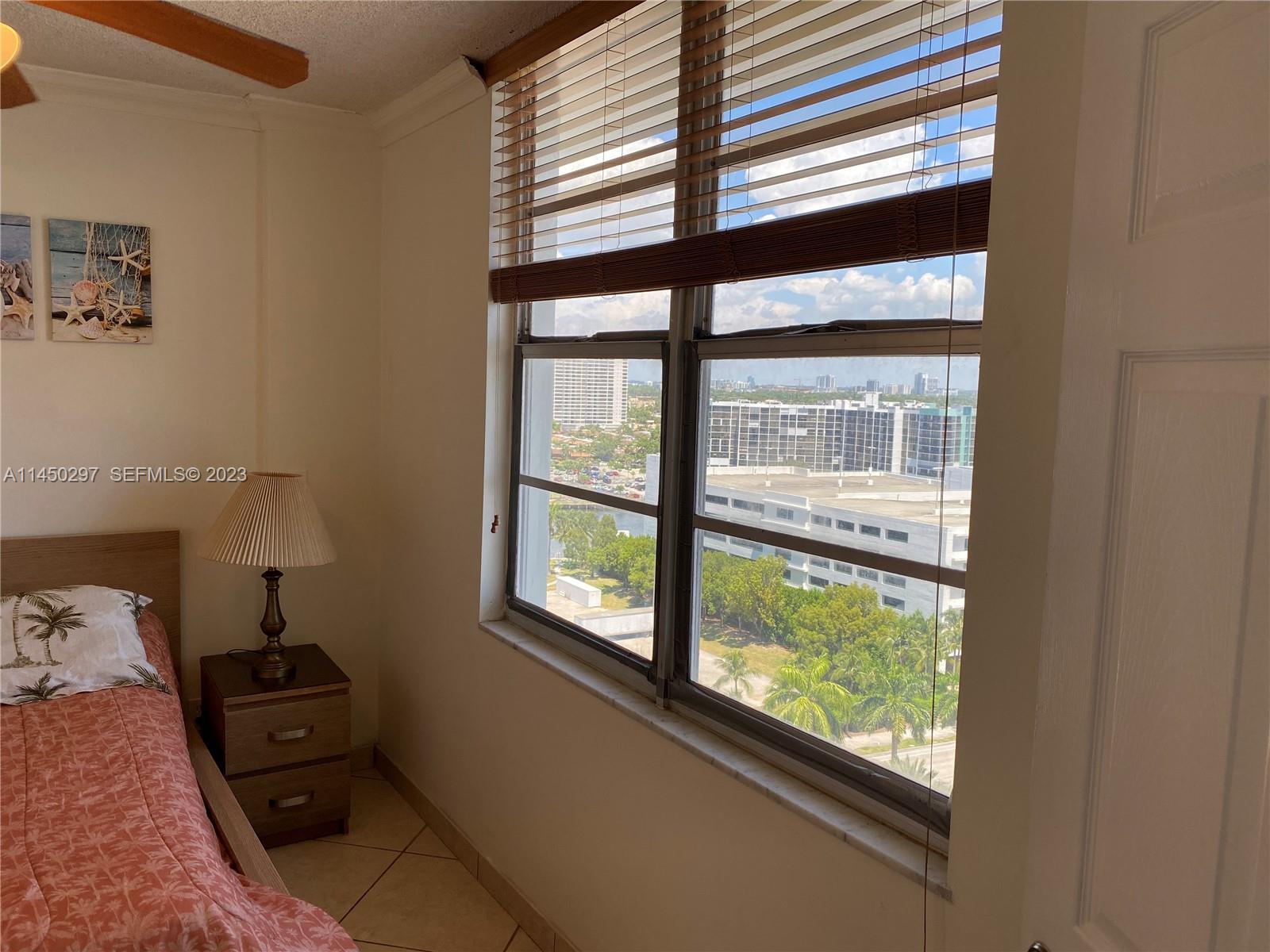 A bedroom features a bed, a nightstand with a lamp, and a window overlooking buildings — 3725 S Ocean Dr # 1521, Hollywood FL 33019, HOLLYWOOD, FL