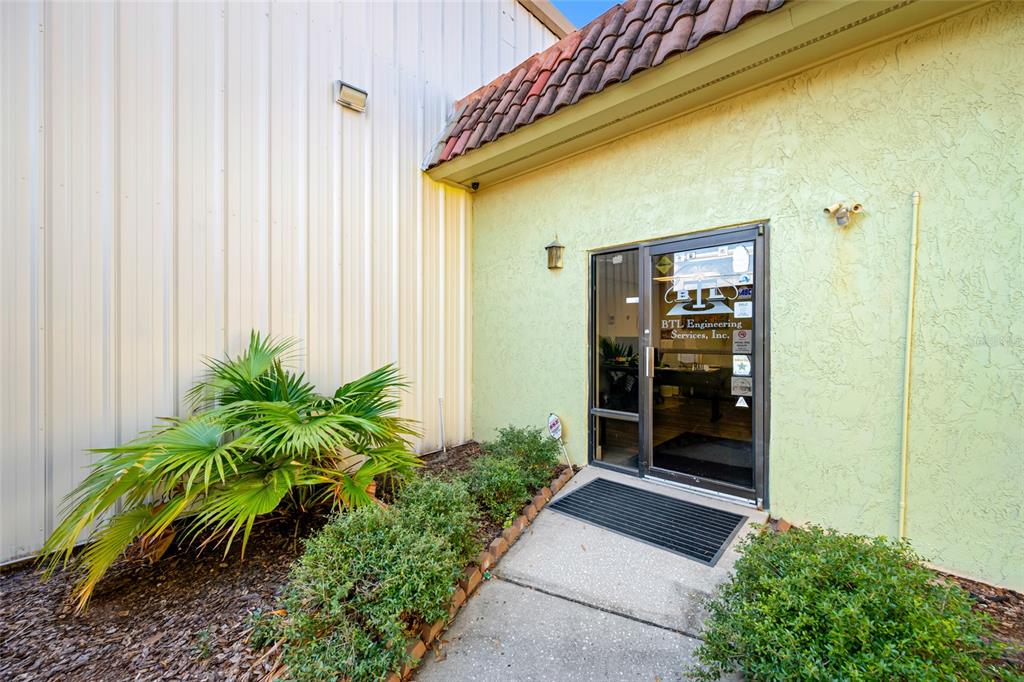The exterior entrance of a commercial building features a glass door, landscaping, and metal siding — 5802 N OCCIDENT STREET, TAMPA, FL