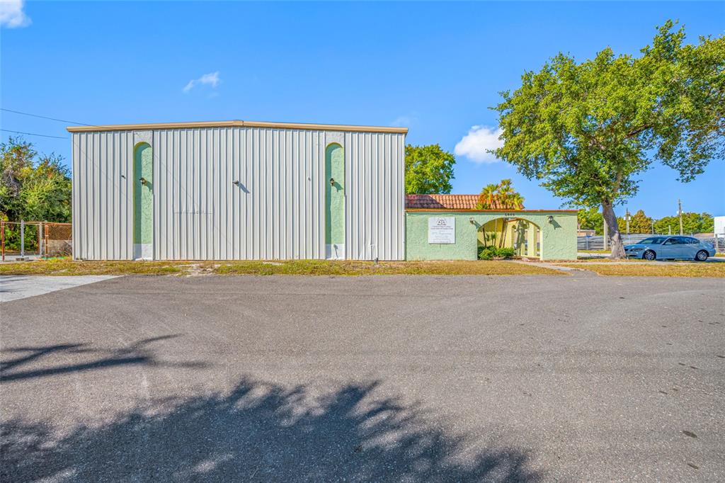 A light-colored metal warehouse building stands next to a small, green stucco office structure — 5802 N OCCIDENT STREET, TAMPA, FL