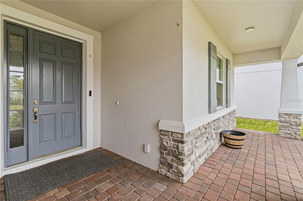 A covered front porch features a gray door, stone veneer accents, and brick pavers — 2510 CEDAR SHAKE COURT, OVIEDO, FL