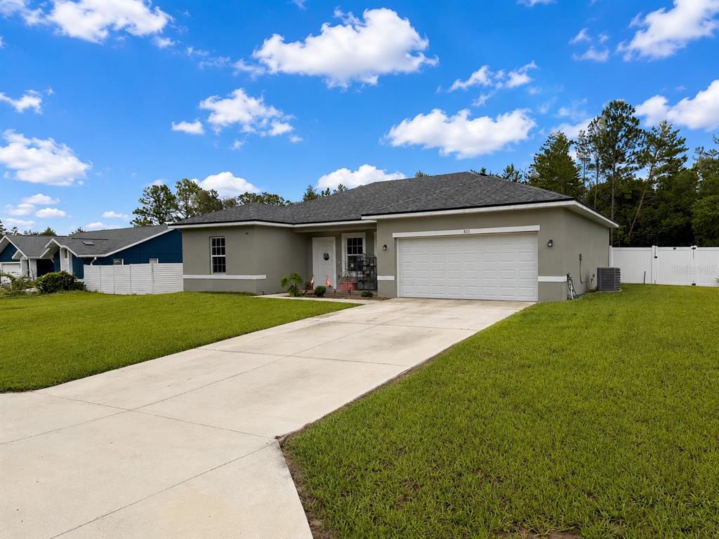 A single-story house with a white garage door, gray exterior, and a concrete driveway — 835 MARION OAKS MANOR, OCALA, FL