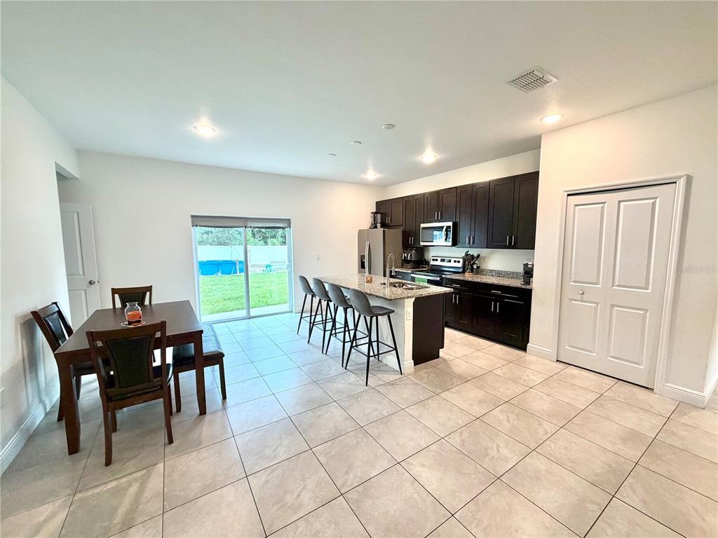 An open-concept kitchen and dining area features dark cabinets, granite countertops, and tile flooring — 835 MARION OAKS MANOR, OCALA, FL