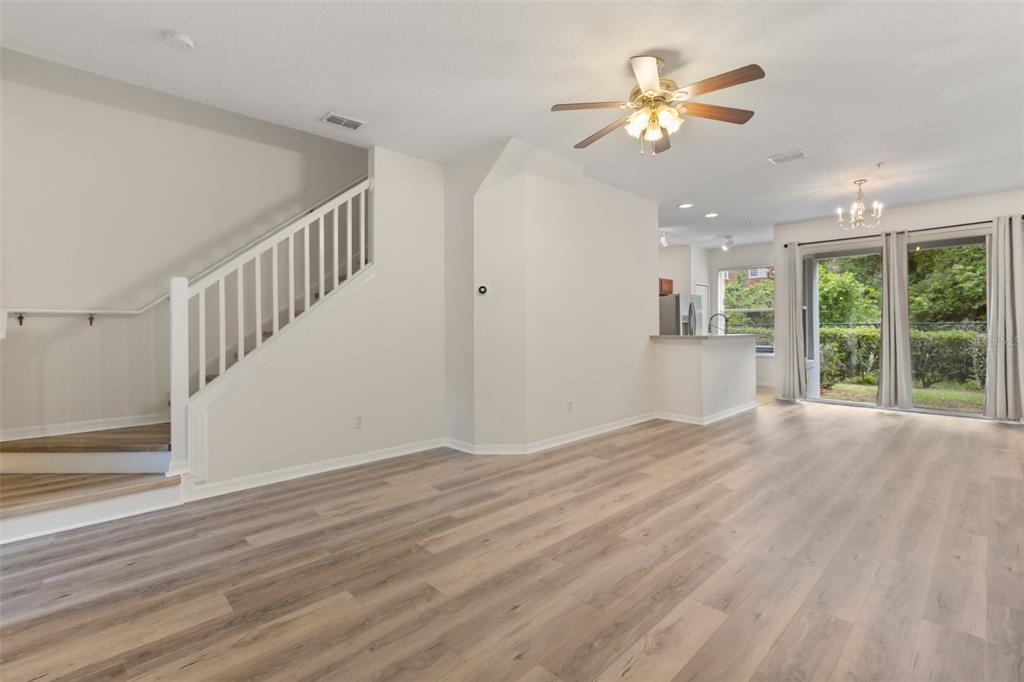 An open-concept living area features light wood-look flooring, a staircase, and sliding glass doors — 520 MAJESTIC WAY, ALTAMONTE SPRINGS, FL